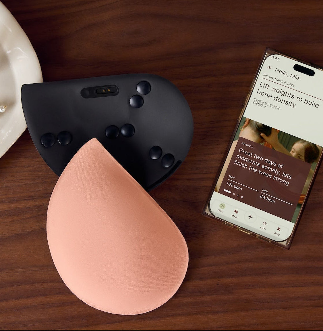 Two silicone breast forms, one pink and one black, on a wooden surface with a smartphone displaying an app.